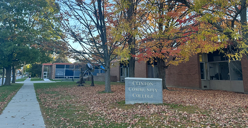 A brick building with fall foliage next to a sign that says 'Clinton Community College'