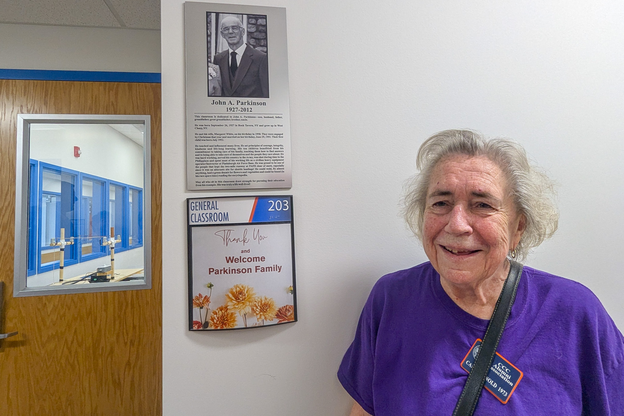 A woman standing in front of a plaque near a classroom in a hallway